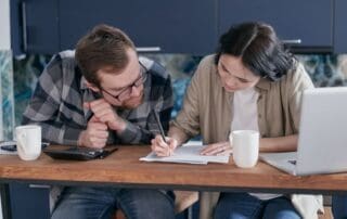 Man reviewing financial documents at kitchen table with laptop and calculator, practicing life skills after rehab