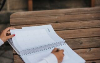 Woman writing in a planner outdoors, staying organized and accountable in sober living during summer.