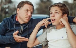 A father and teenage son having a serious conversation outdoors, representing family recovery boundaries and open communication.
